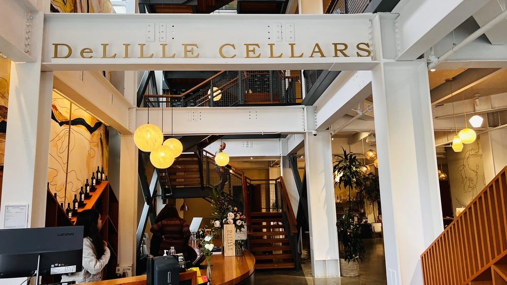 DeLille Cellars interior with exposed white beams, warm pendant lighting, and wood stairs